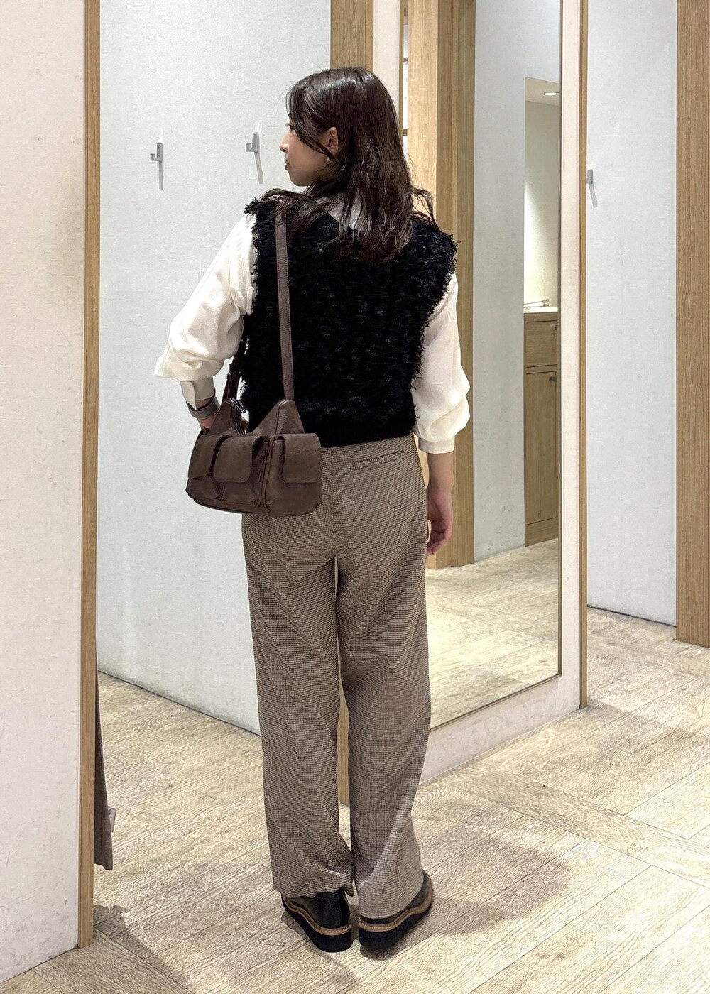 ベージュ系のスラックス、ブラウン系のショルダーバッグ、ブラック系のベストを着用したレディースの秋コーディネートの3枚目の写真