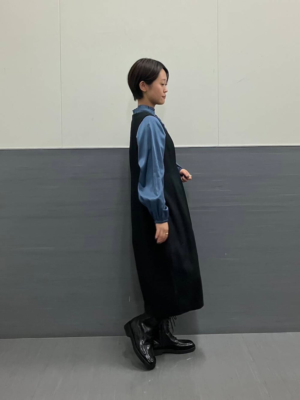 ブルー系のシャツ/ブラウス、ブラック系のジャンパースカート、ブラック系のブーツを着用したレディースの秋コーディネートの2枚目の写真