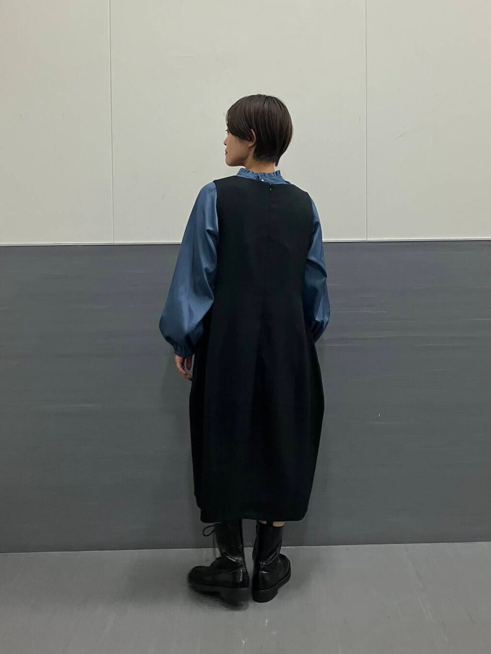 ブルー系のシャツ/ブラウス、ブラック系のジャンパースカート、ブラック系のブーツを着用したレディースの秋コーディネートの3枚目の写真