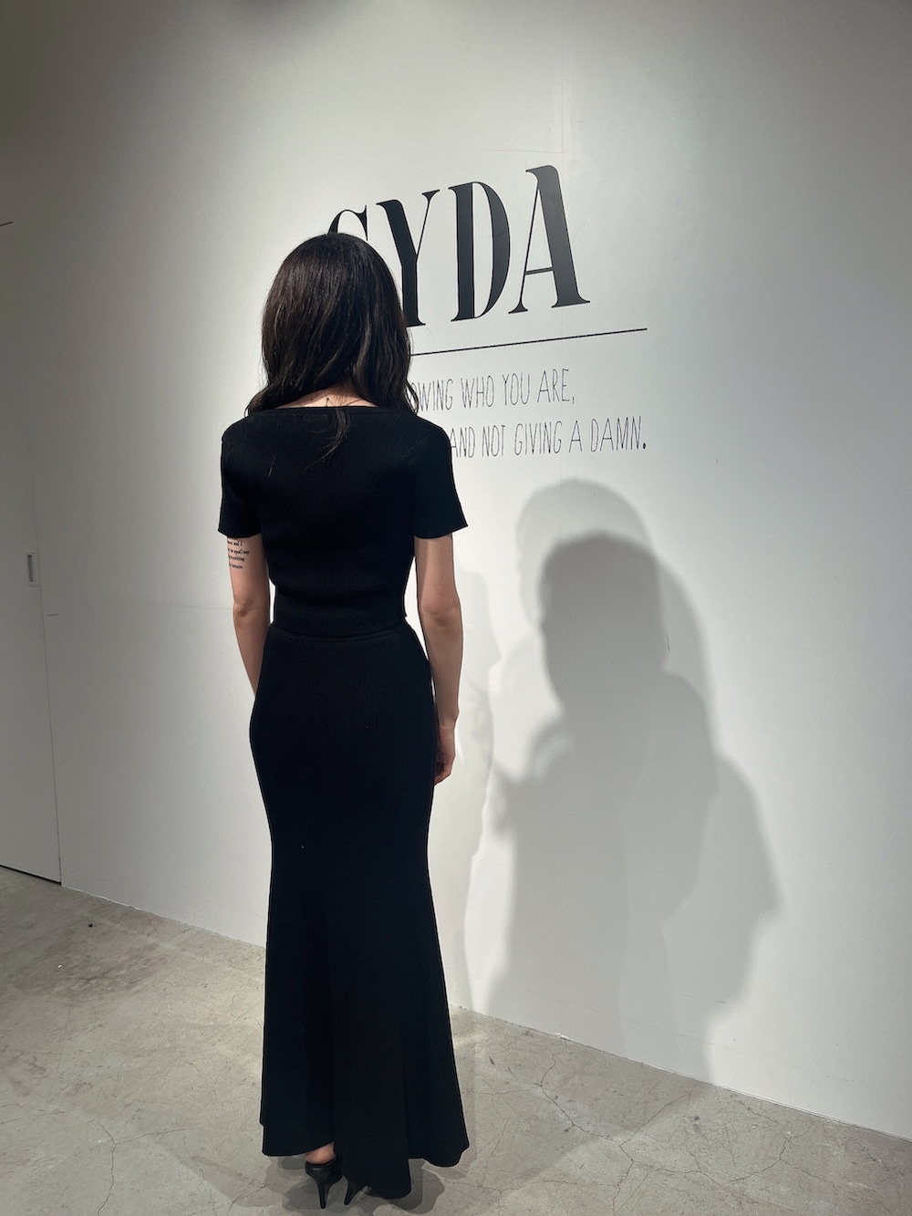 ブラック系のニット/セーター、ブラック系のスカート、ブラック系のパンプスを着用したレディースの夏コーディネートの3枚目の写真