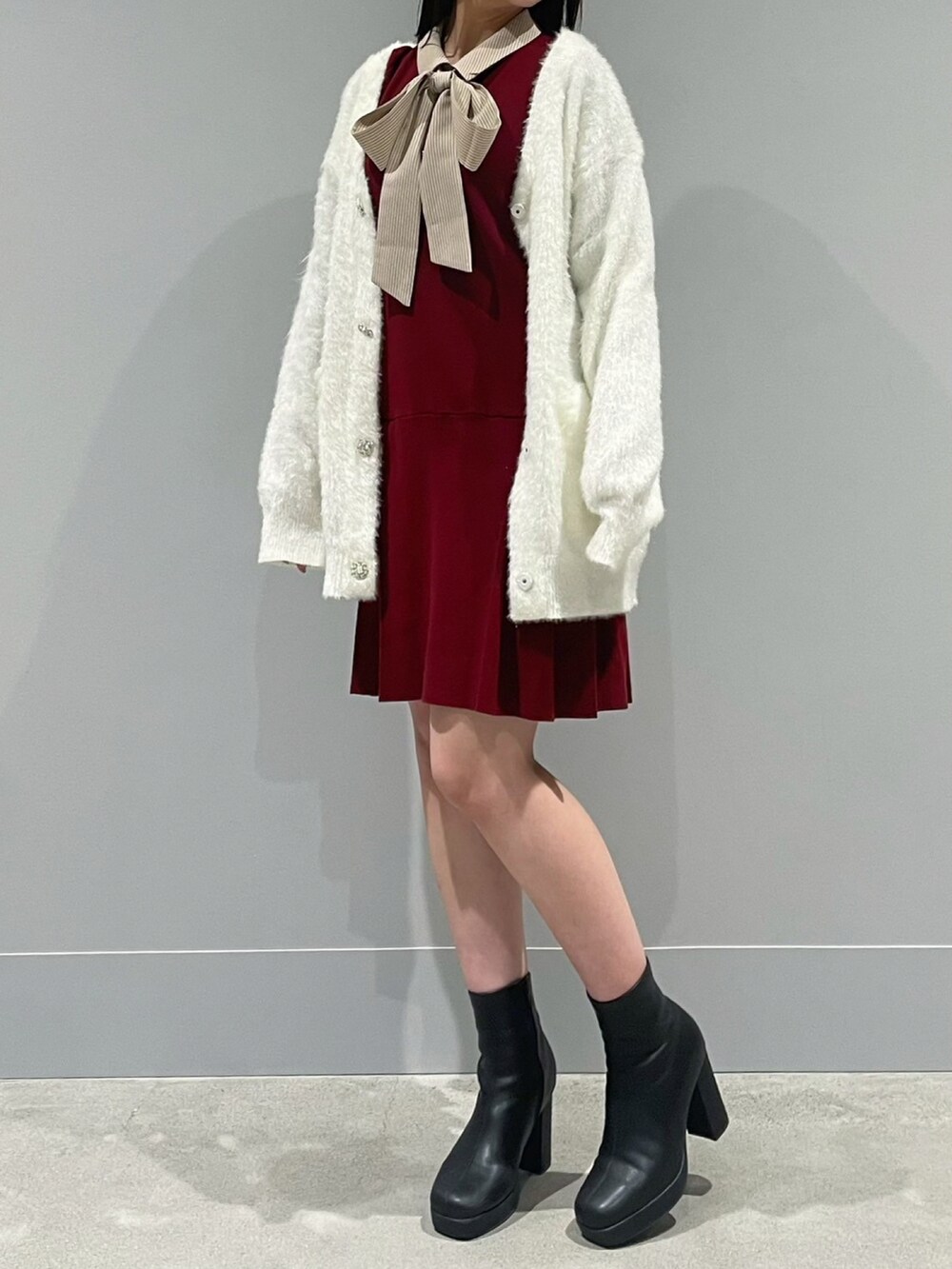 ホワイト系のカーディガン/ボレロ、レッド系のワンピース、ブラック系のブーツを着用したレディースの冬コーディネートの2枚目の写真