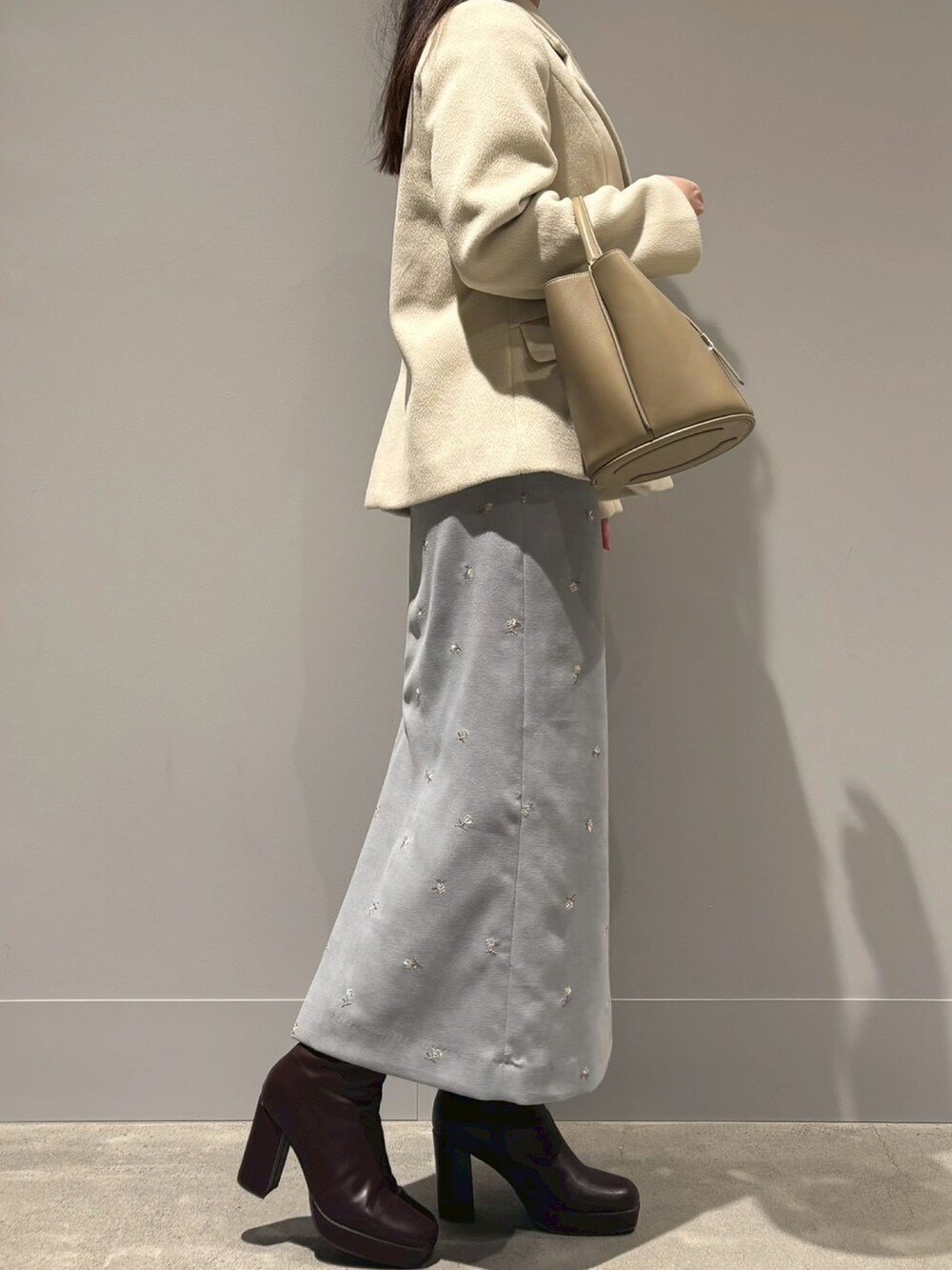 ブルー系のスカート、ベージュ系のハンドバッグ、ブラウン系のジャケット/アウターを着用したレディースの冬コーディネートの2枚目の写真