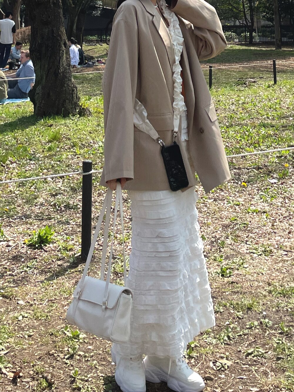 ベージュ系のテーラードジャケット、ホワイト系のスカート、ホワイト系のショルダーバッグを着用したレディースの春コーディネートの2枚目の写真