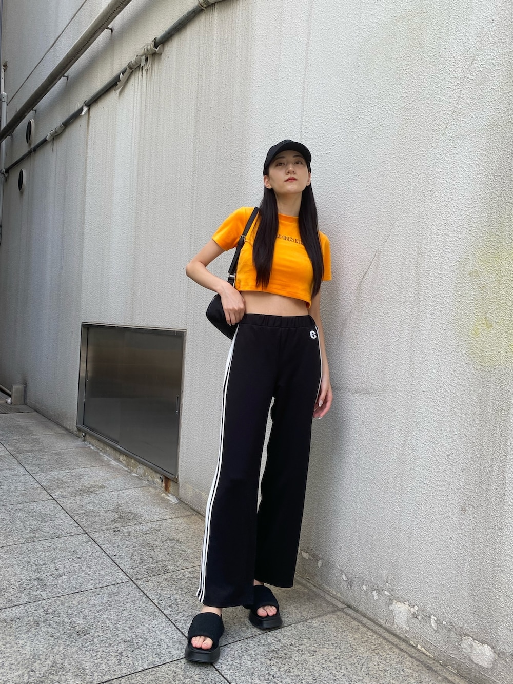 ブラック系のその他パンツ、ブラック系のハンドバッグ、オレンジ系のTシャツ/カットソーを着用したレディースの夏コーディネートの2枚目の写真