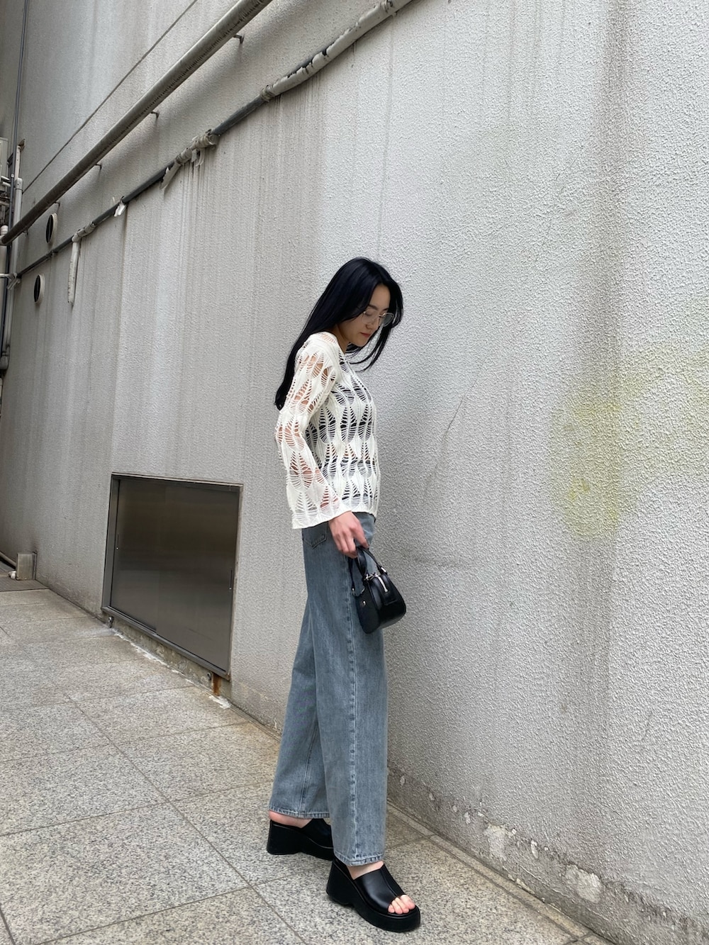 ブラック系のハンドバッグ、ブラック系のサンダル、ブルー系のデニムパンツを着用したレディースの春コーディネートの4枚目の写真