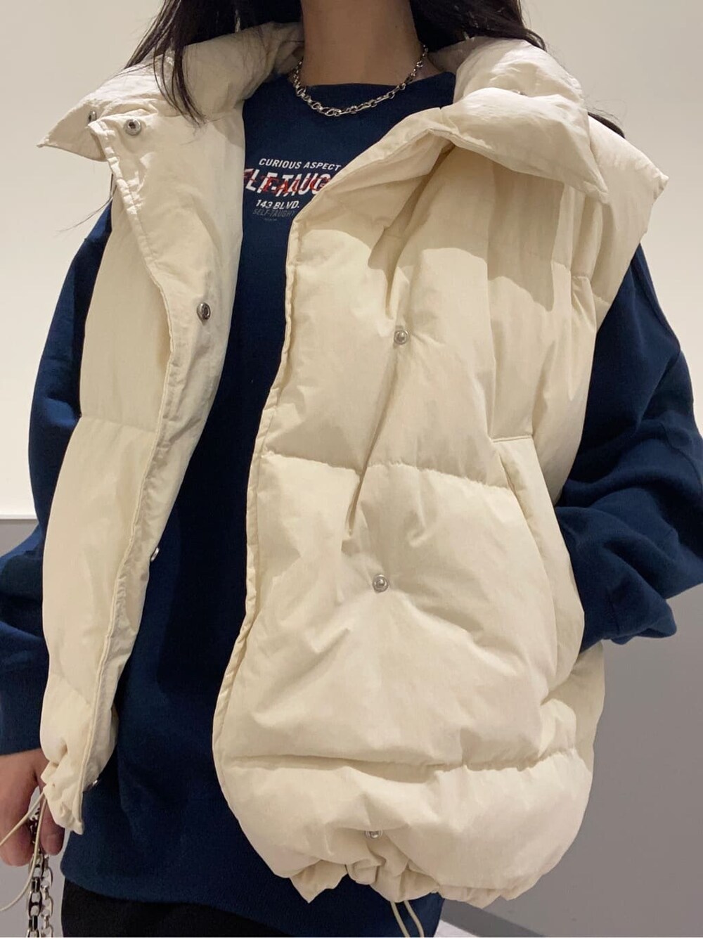 ブラック系のスカート、ホワイト系のダウンベスト、ブルー系のスウェットを着用したレディースの秋コーディネートの6枚目の写真