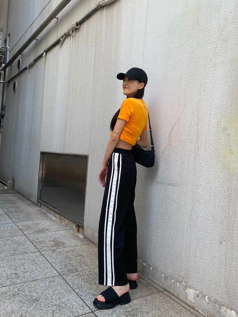 ブラック系のその他パンツ、ブラック系のハンドバッグ、オレンジ系のTシャツ/カットソーを着用したレディースの夏コーディネートの4枚目の写真