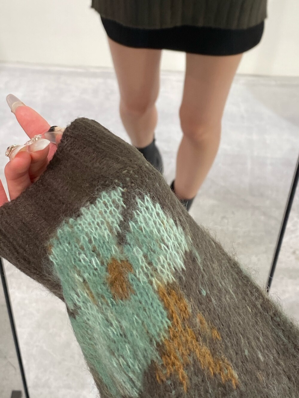 グリーン系のニット/セーター、ブラック系のスカート、ブラック系のブーツを着用したレディースの秋コーディネートの4枚目の写真