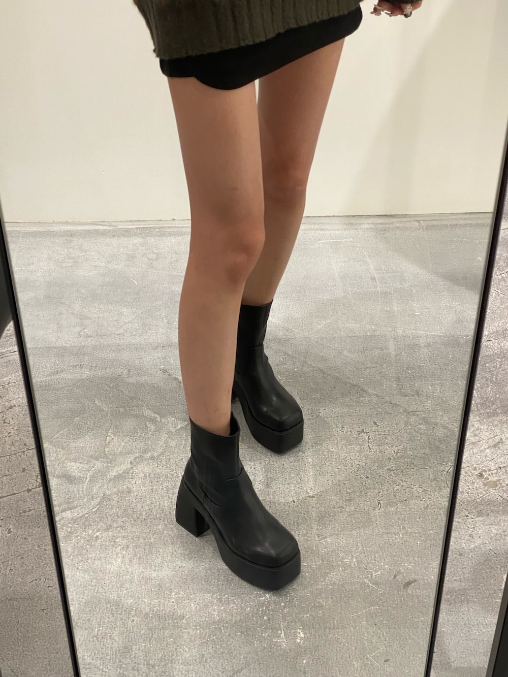 グリーン系のニット/セーター、ブラック系のスカート、ブラック系のブーツを着用したレディースの秋コーディネートの6枚目の写真