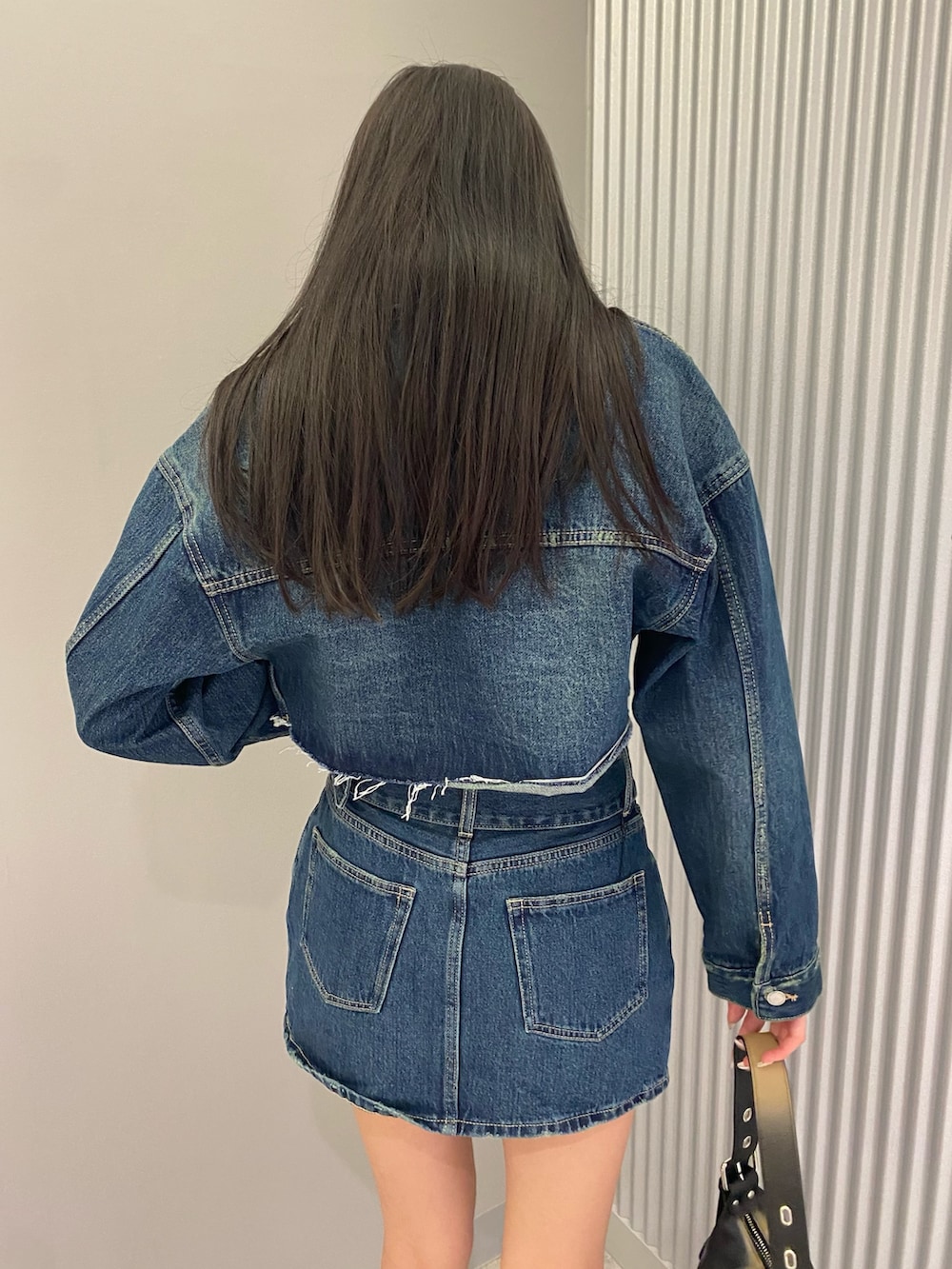 ブルー系のデニムジャケット、ブルー系のデニムスカート、ブラック系のハンドバッグを着用したレディースの夏コーディネートの6枚目の写真