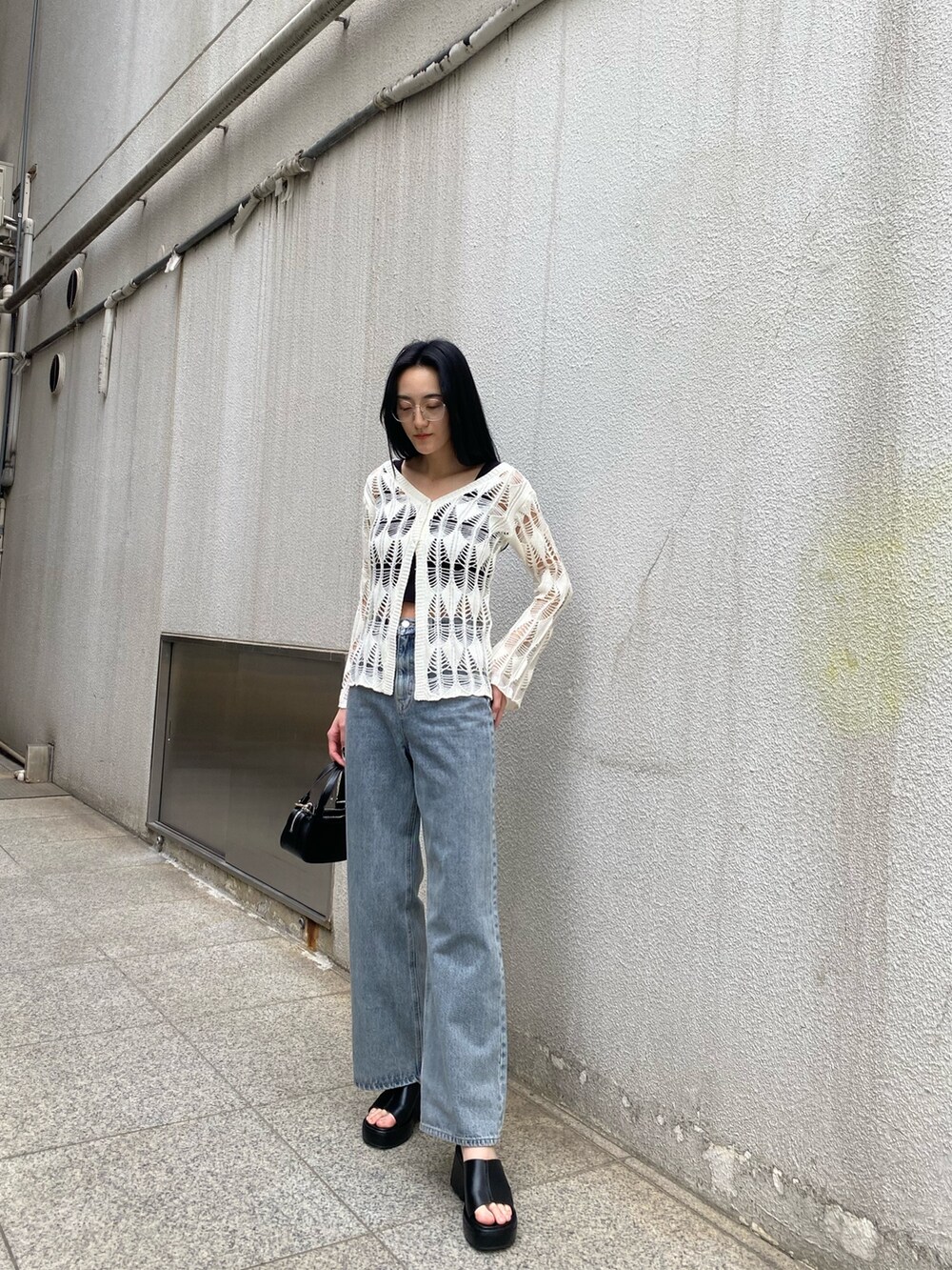 ブラック系のハンドバッグ、ブラック系のサンダル、ブルー系のデニムパンツを着用したレディースの春コーディネートの2枚目の写真