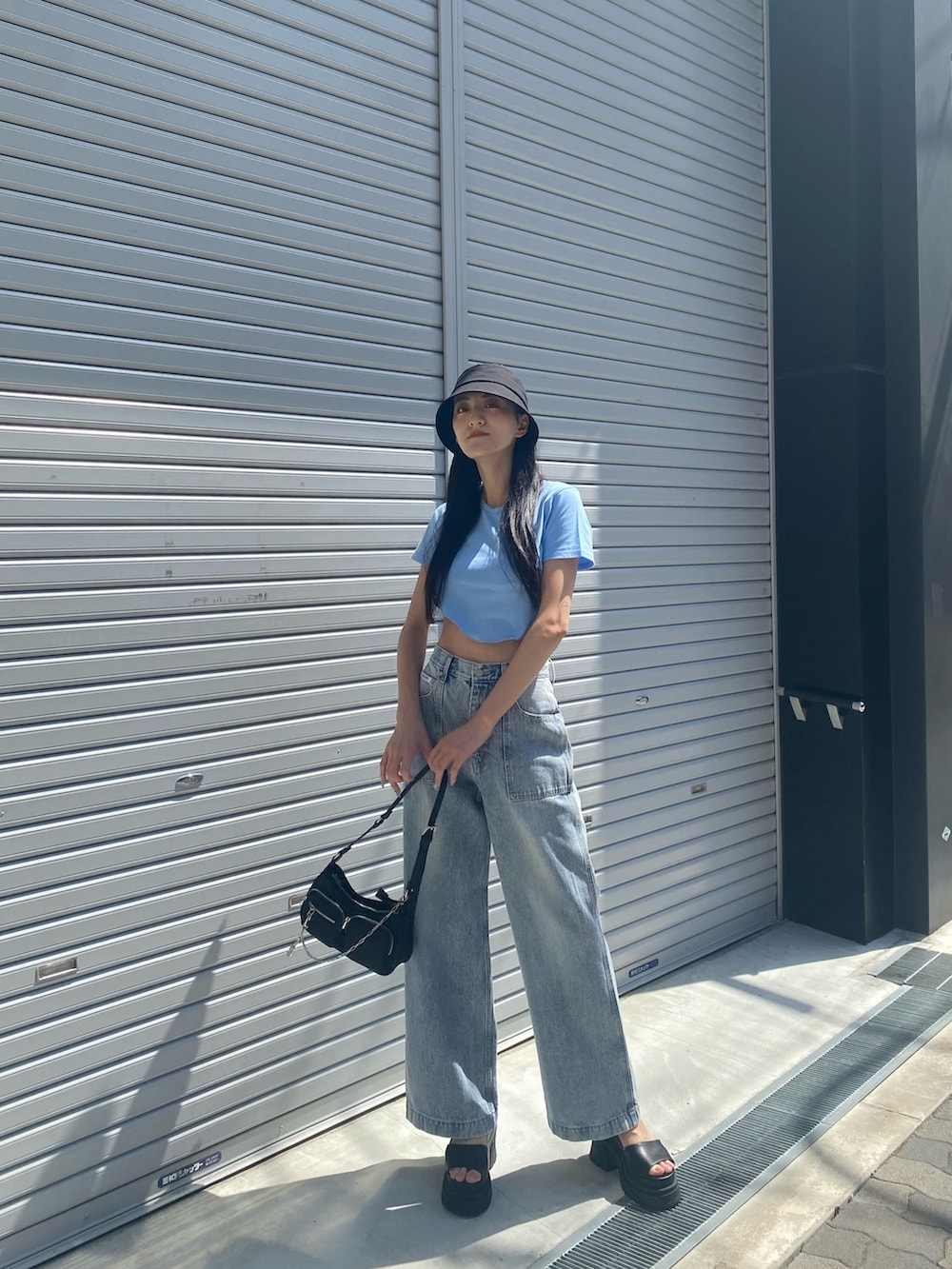 ブルー系のデニムパンツ、ブラック系のサンダル、ブラック系のハンドバッグを着用したレディースの夏コーディネートの4枚目の写真