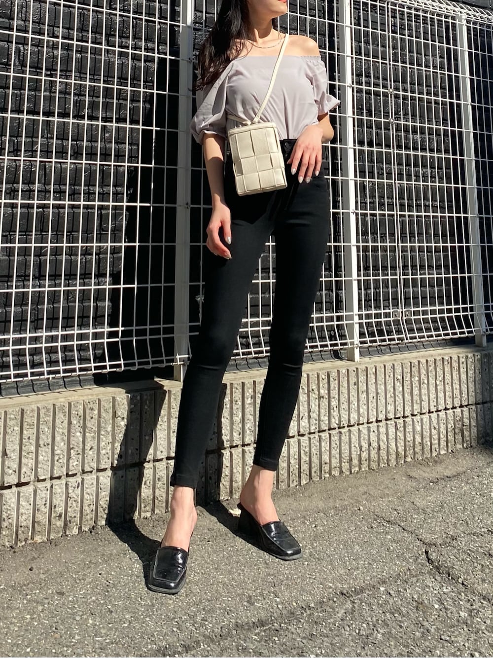 ホワイト系のショルダーバッグ、ブラック系のサンダル、ブラック系のデニムパンツを着用したレディースの春コーディネートの2枚目の写真