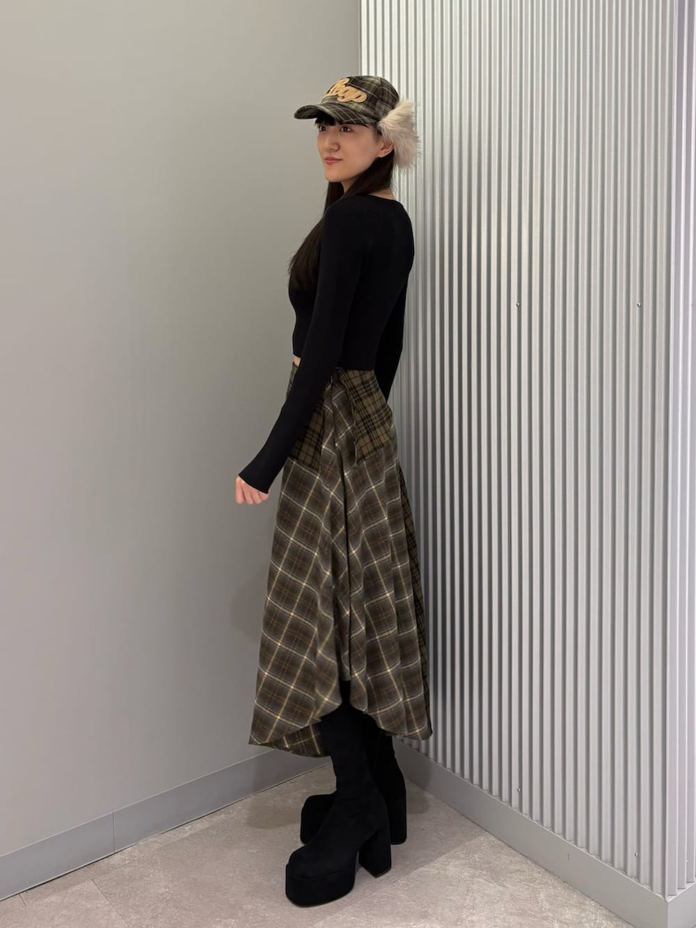 グリーン系のスカート、ブラック系のニット/セーター、ブラック系のブーツを着用したレディースの秋コーディネートの3枚目の写真