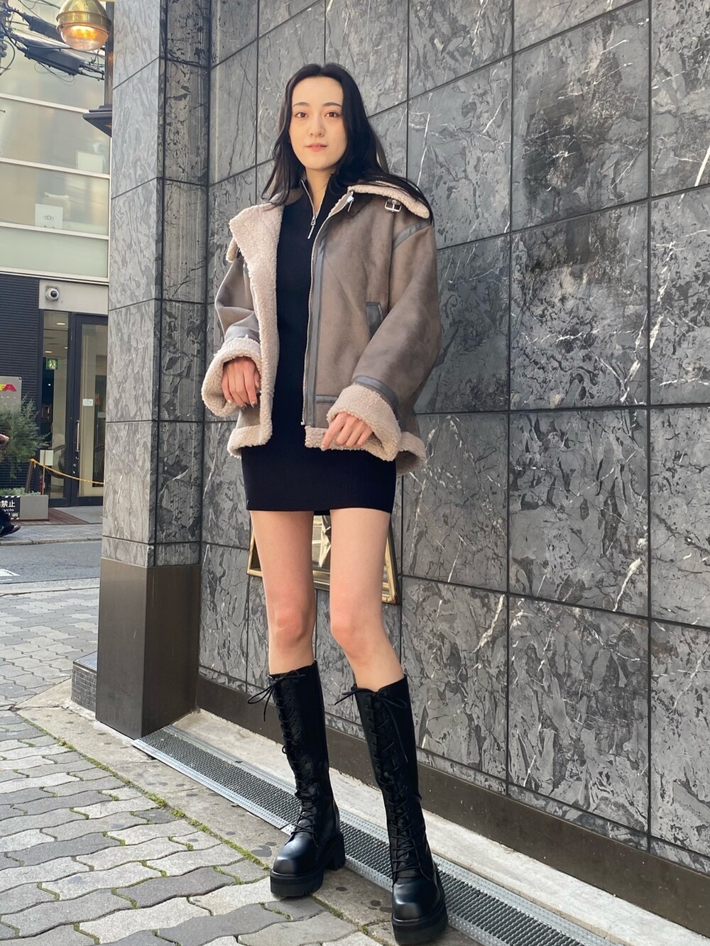 グレー系のブルゾン、ブラック系のワンピース、ブラック系のブーツを着用したレディースの冬コーディネートの2枚目の写真