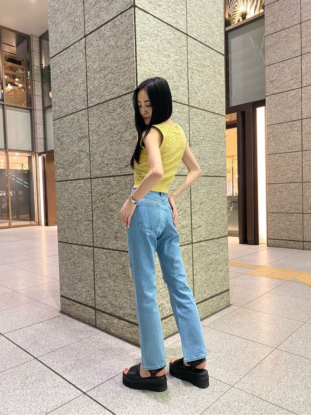 イエロー系のタンクトップ、ブルー系のデニムパンツ、ブラック系のサンダルを着用したレディースの夏コーディネートの2枚目の写真