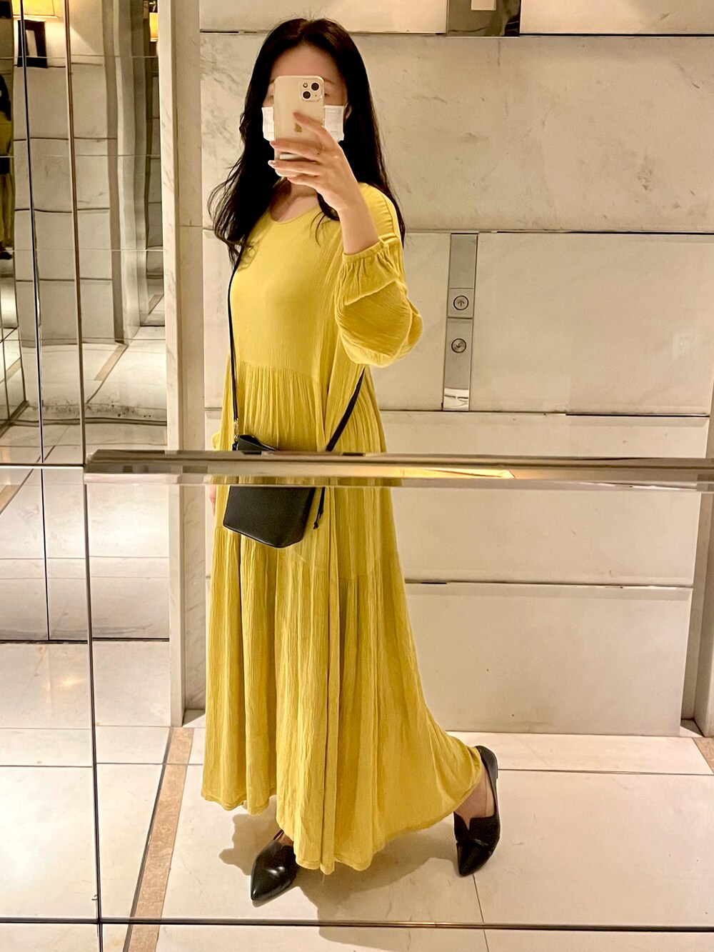 イエロー系のワンピース、ブラック系のパンプス、ブラック系のショルダーバッグを着用したレディースの秋コーディネートの2枚目の写真