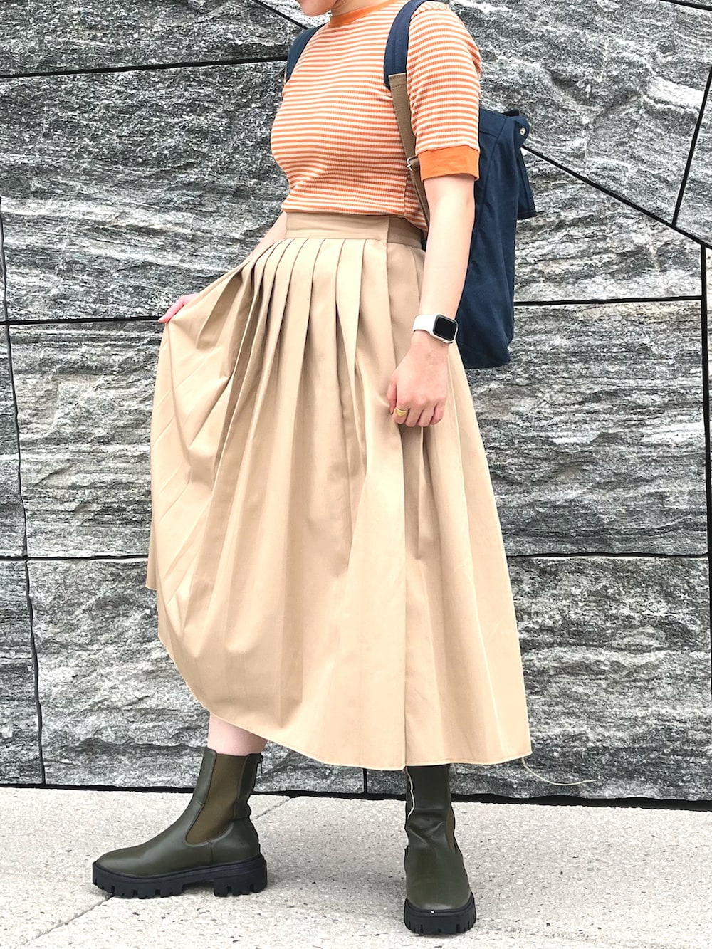 ベージュ系のスカート、オレンジ系のTシャツ/カットソー、グリーン系のブーツを着用したレディースの春コーディネートの2枚目の写真