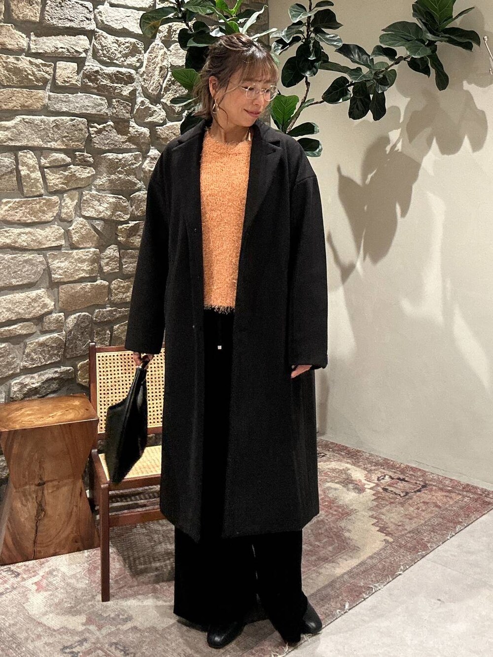 ブラック系のブーツ、ブラック系のチェスターコート、オレンジ系のニット/セーターを着用したレディースの冬コーディネートの2枚目の写真