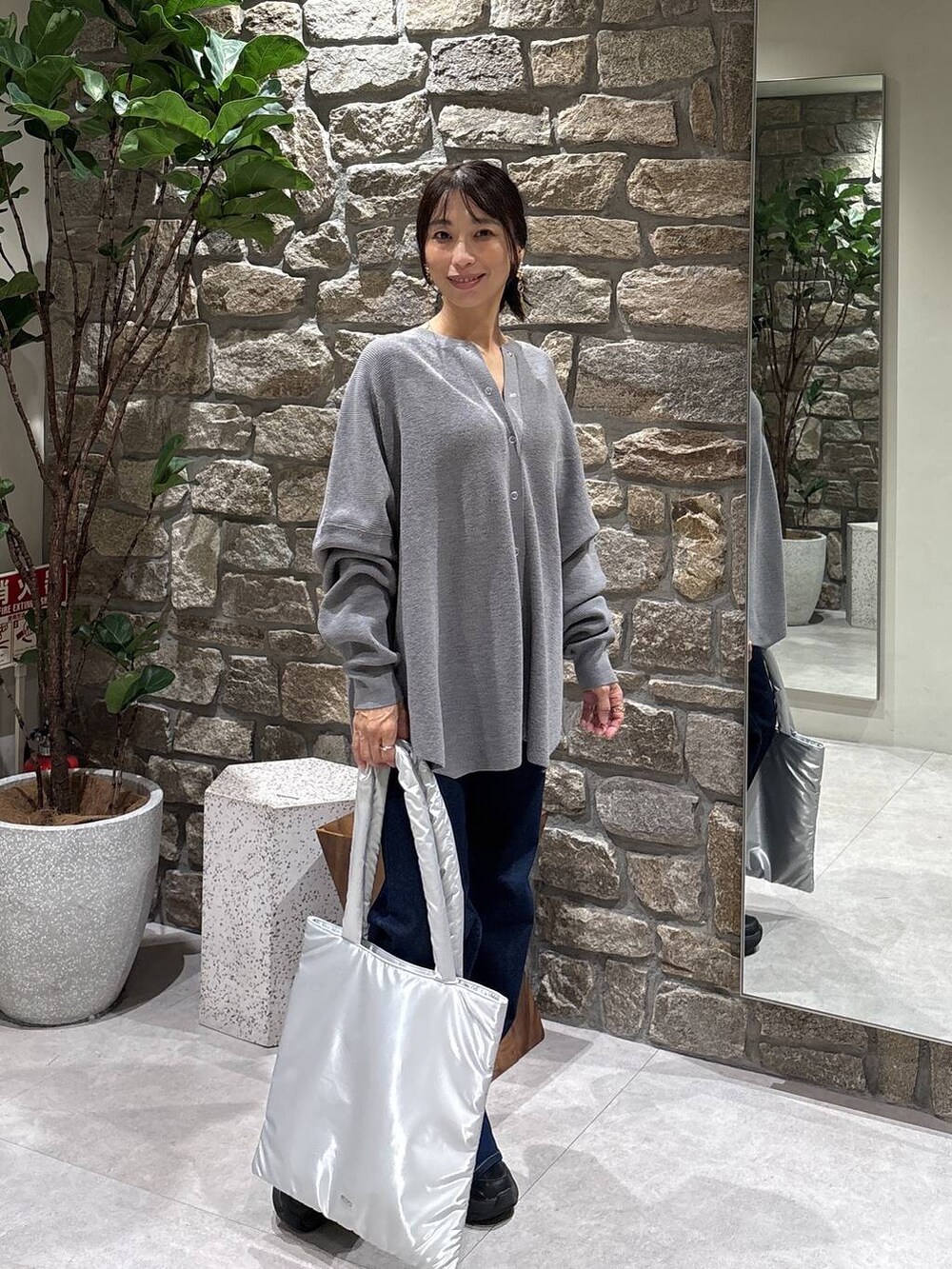 シルバー系のトートバッグ、ブルー系のデニムパンツ、グレー系のニット/セーターを着用したレディースの秋コーディネートの3枚目の写真