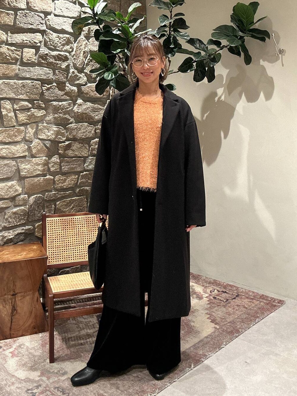 ブラック系のブーツ、ブラック系のチェスターコート、オレンジ系のニット/セーターを着用したレディースの冬コーディネートの3枚目の写真