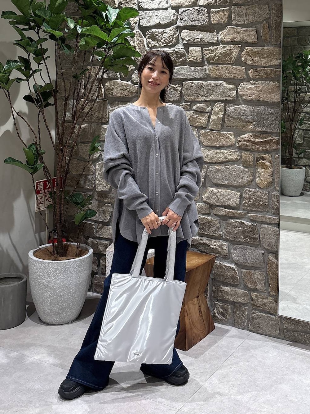 シルバー系のトートバッグ、ブルー系のデニムパンツ、グレー系のニット/セーターを着用したレディースの秋コーディネートの2枚目の写真