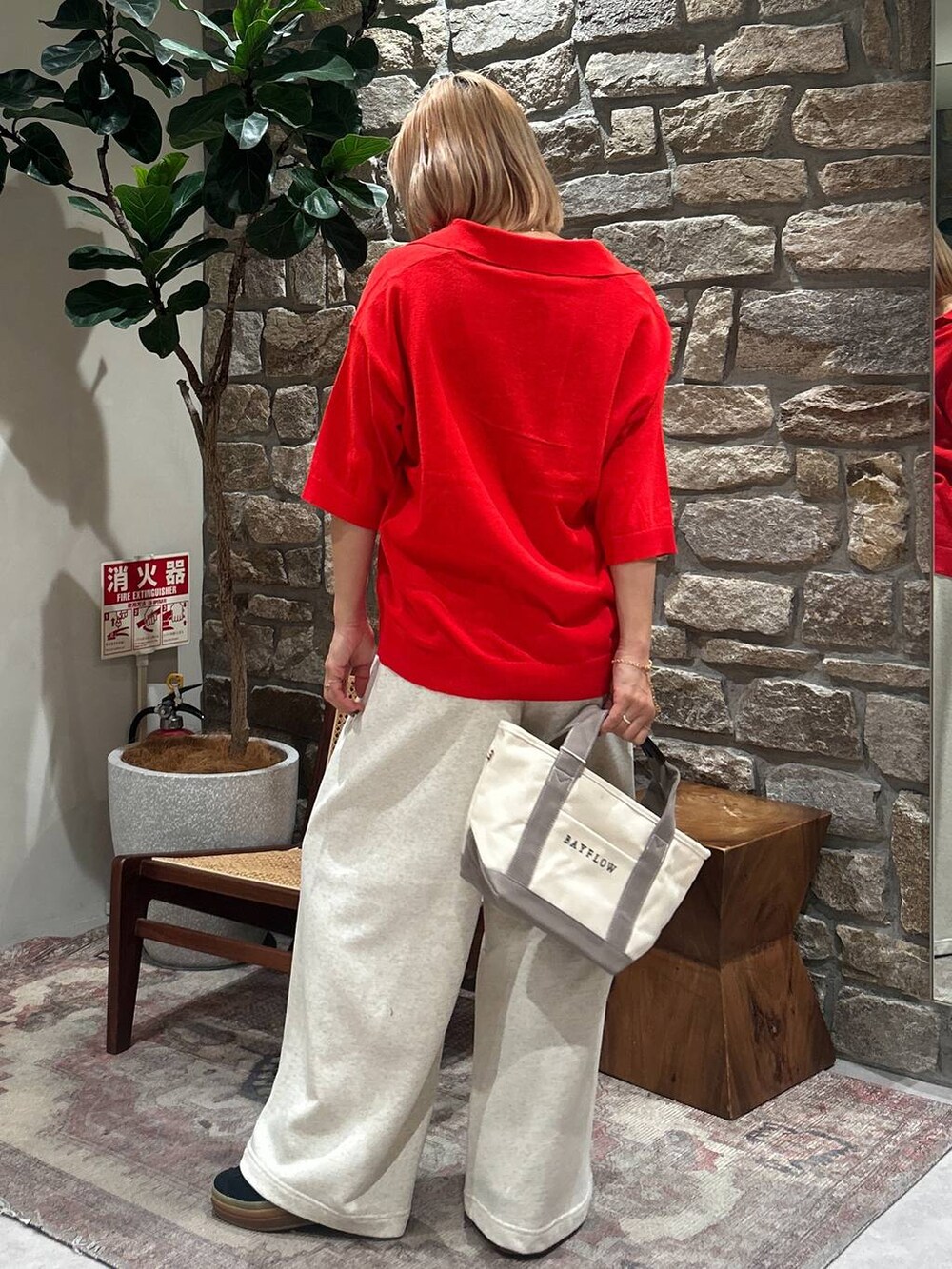 レッド系のニット/セーター、ベージュ系のトートバッグ、ベージュ系のスウェットパンツを着用したレディースの春コーディネートの3枚目の写真