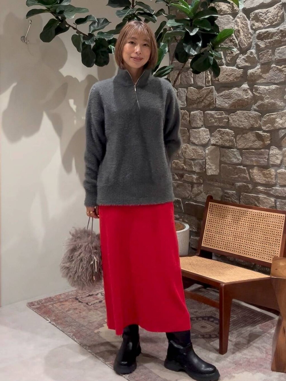 レッド系のスカート、グレー系のニット/セーター、ブラック系のブーツを着用したレディースの秋コーディネートの2枚目の写真