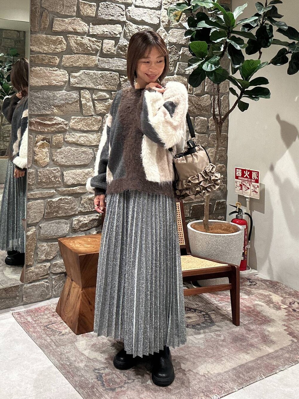 ブラウン系のニット/セーター、ブラック系のブーツ、シルバー系のスカートを着用したレディースの冬コーディネートの3枚目の写真