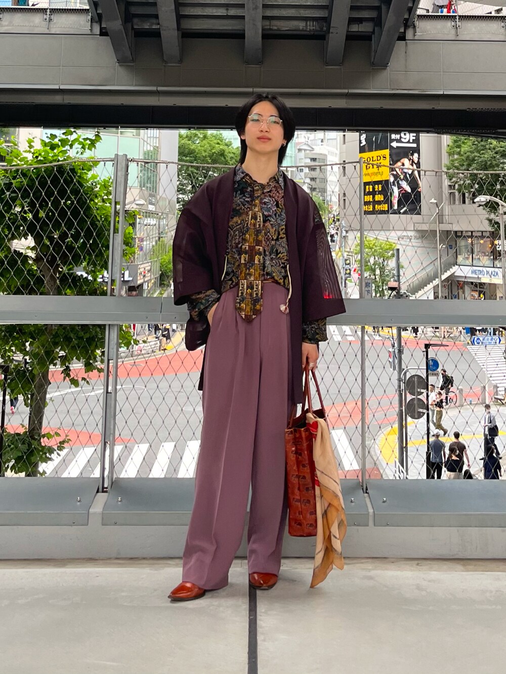 パープル系のスラックス、オレンジ系のトートバッグ、オレンジ系のブーツを着用したメンズの夏コーディネートの2枚目の写真