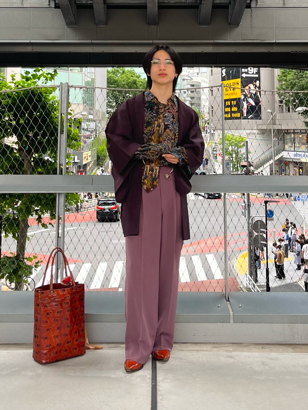 パープル系のスラックス、オレンジ系のトートバッグ、オレンジ系のブーツを着用したメンズの夏コーディネートの3枚目の写真