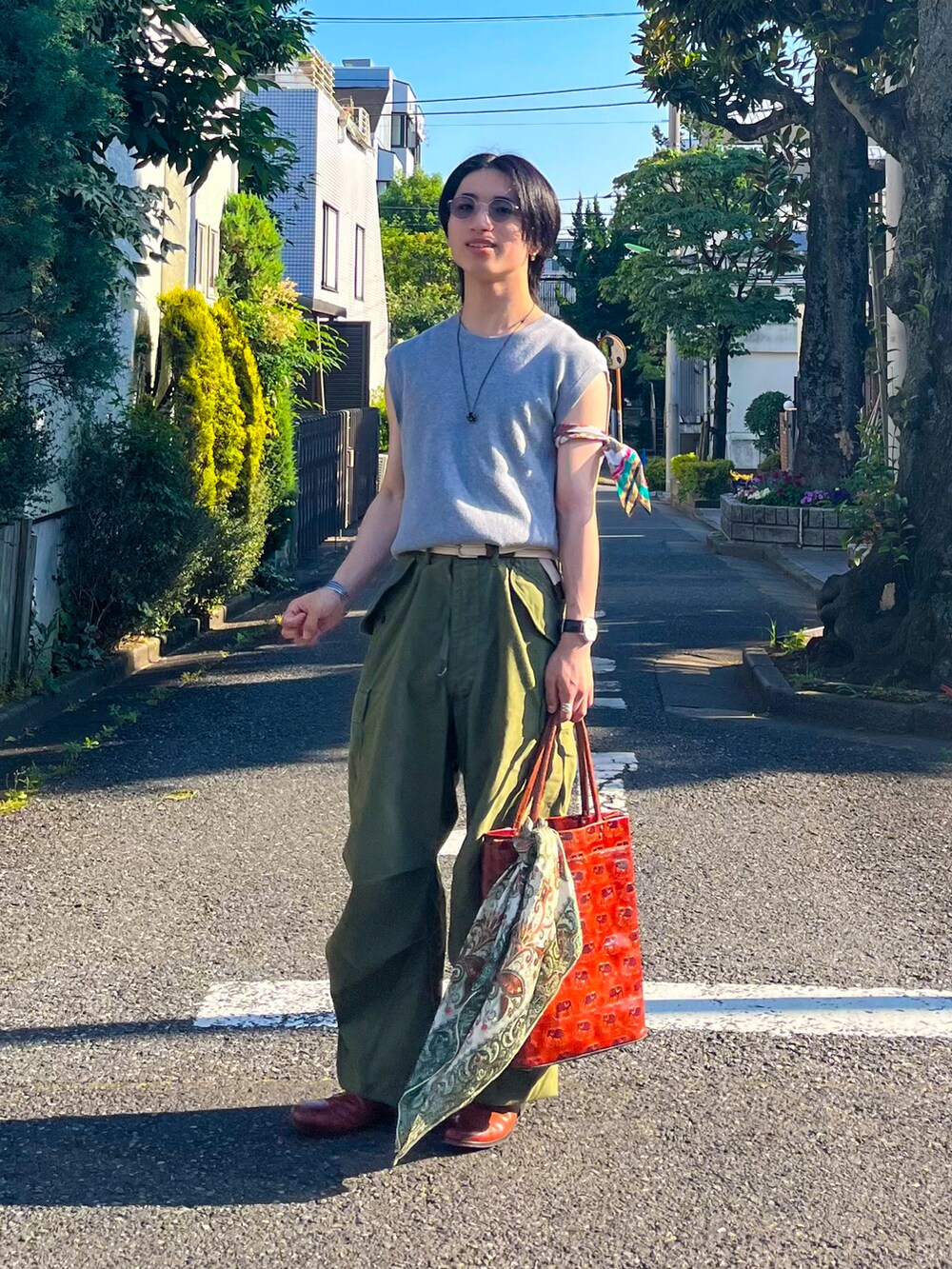 グレー系のベスト、オレンジ系のトートバッグ、グリーン系のカーゴパンツを着用したメンズの夏コーディネートの3枚目の写真