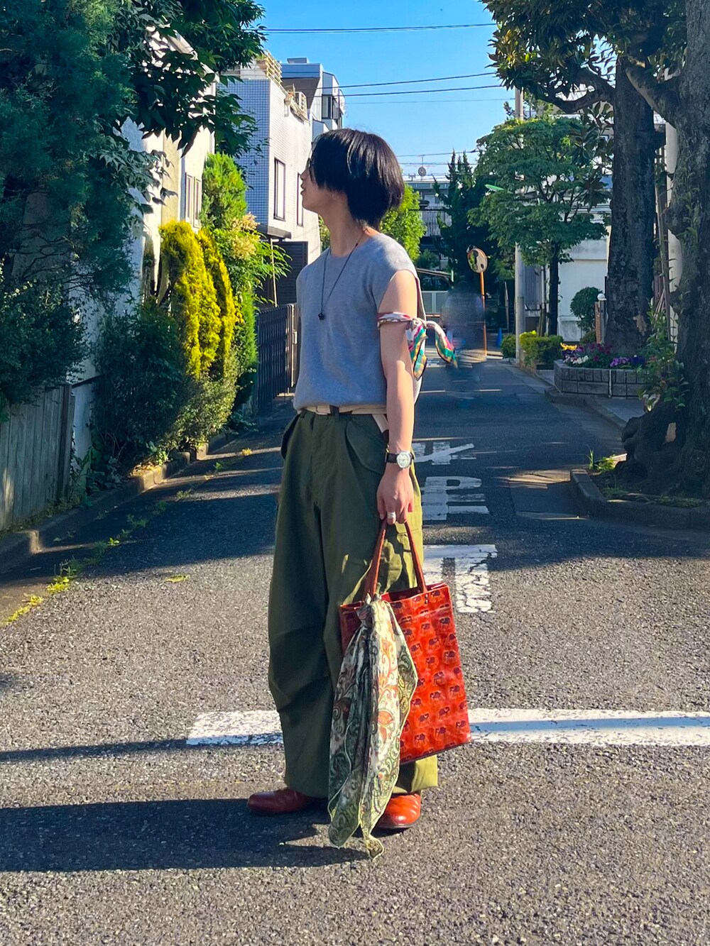 グレー系のベスト、オレンジ系のトートバッグ、グリーン系のカーゴパンツを着用したメンズの夏コーディネートの2枚目の写真
