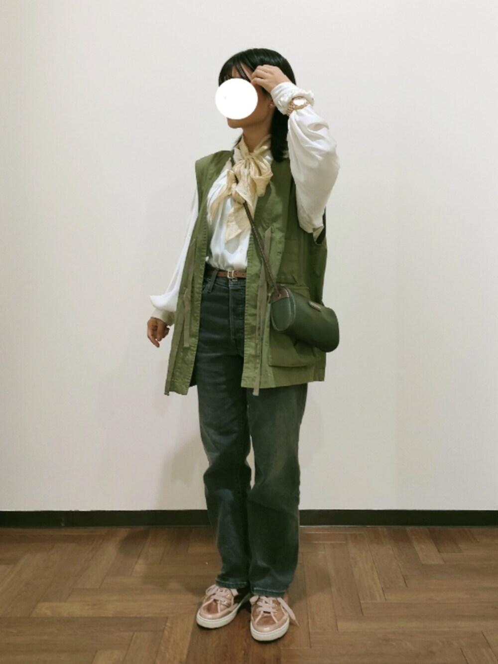 グレー系のデニムパンツ、ピンク系のスニーカー、グリーン系のベストを着用したレディースの秋コーディネートの2枚目の写真