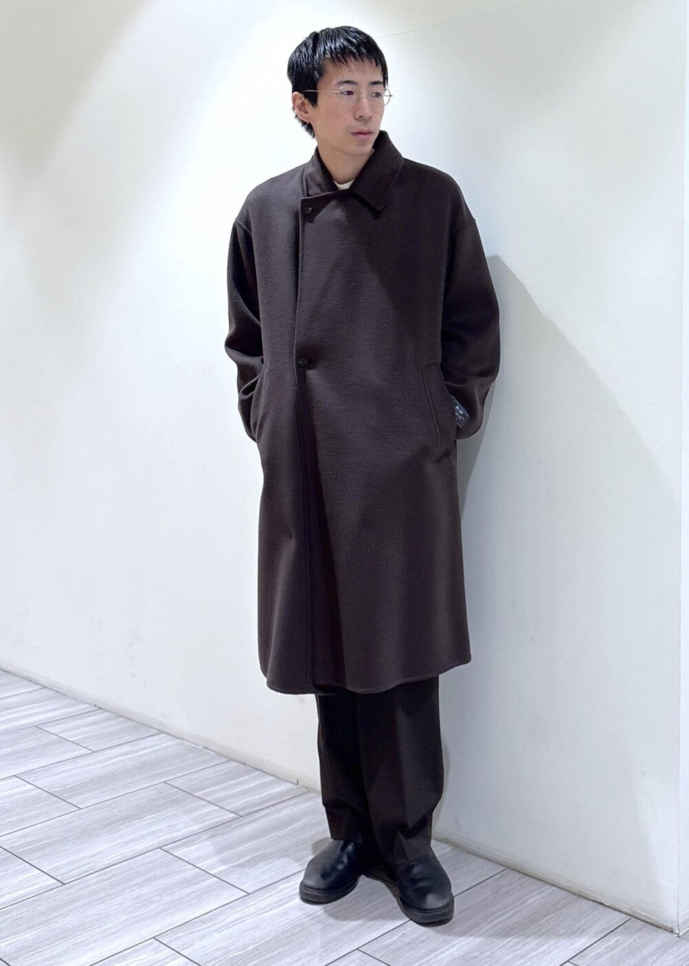 ブラウン系のスラックス、ブラウン系のステンカラーコート、ホワイト系のTシャツ/カットソーを着用したメンズの秋コーディネートの2枚目の写真