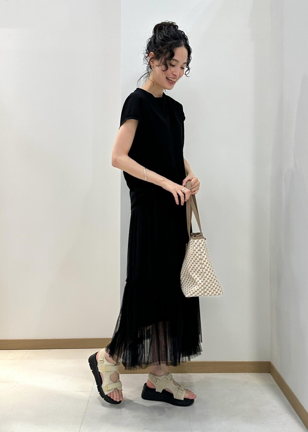 ベージュ系のトートバッグ、ホワイト系のサンダル、ブラック系のTシャツ/カットソーを着用したレディースの夏コーディネートの2枚目の写真