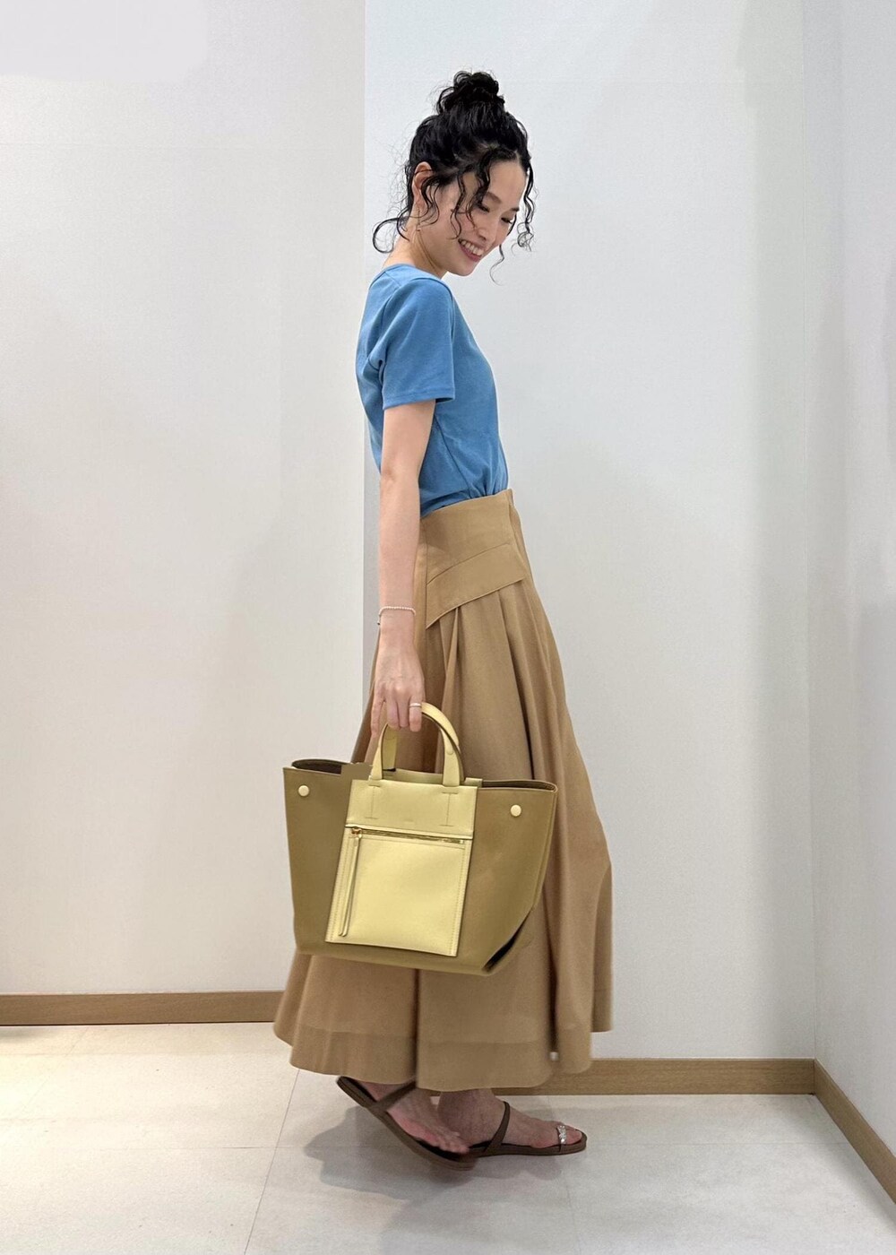 イエロー系のハンドバッグ、ベージュ系のサンダル、ベージュ系のスカートを着用したレディースの夏コーディネートの2枚目の写真