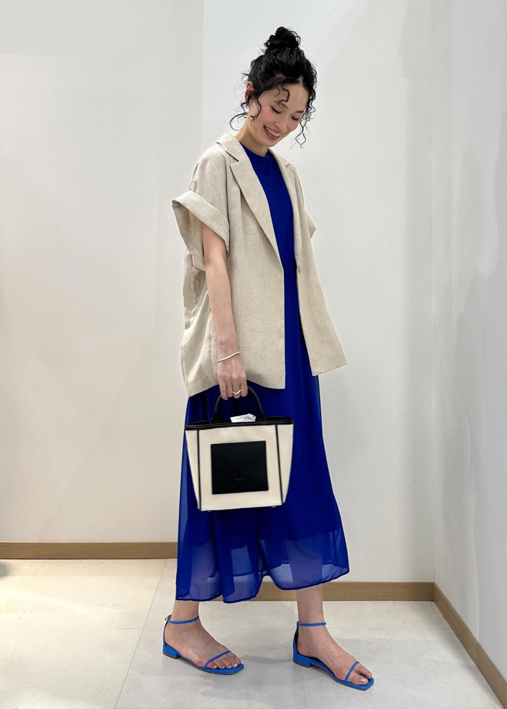 ブラック系のトートバッグ、ブルー系のサンダル、ブルー系のワンピースを着用したレディースの春コーディネートの2枚目の写真