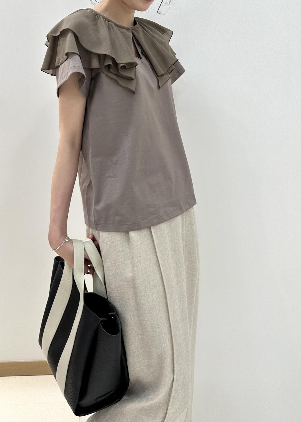 ブラック系のトートバッグ、ブラック系のサンダル、ベージュ系のTシャツ/カットソーを着用したレディースの夏コーディネートの5枚目の写真