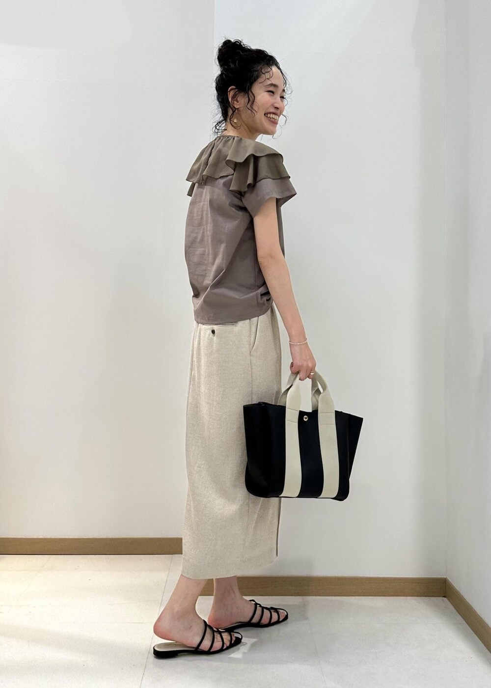 ブラック系のトートバッグ、ブラック系のサンダル、ベージュ系のTシャツ/カットソーを着用したレディースの夏コーディネートの2枚目の写真