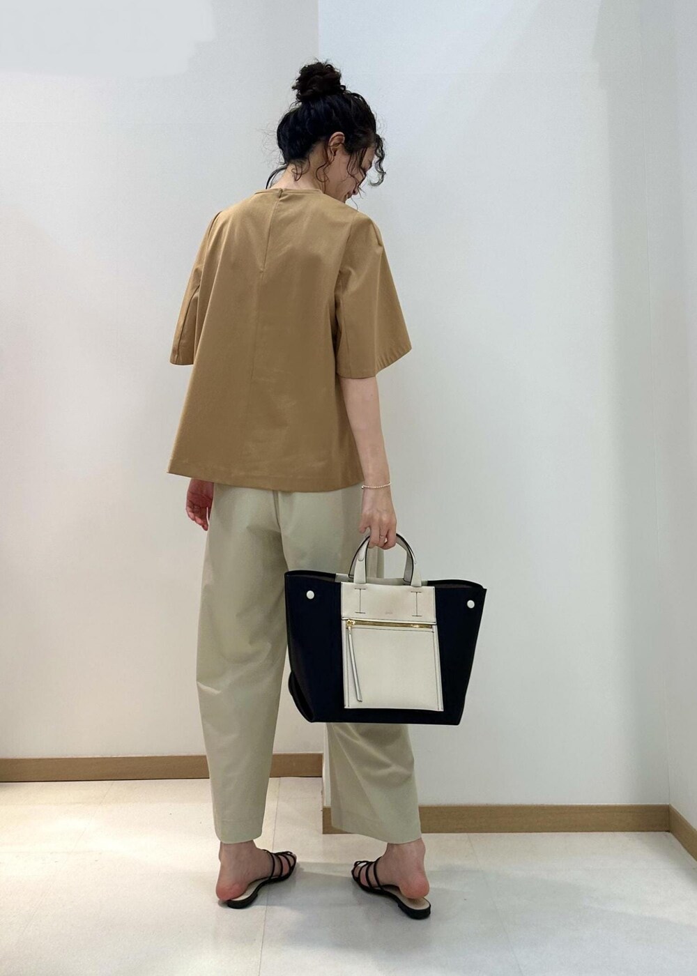 ブラック系のハンドバッグ、ブラック系のサンダル、ベージュ系のTシャツ/カットソーを着用したレディースの夏コーディネートの3枚目の写真