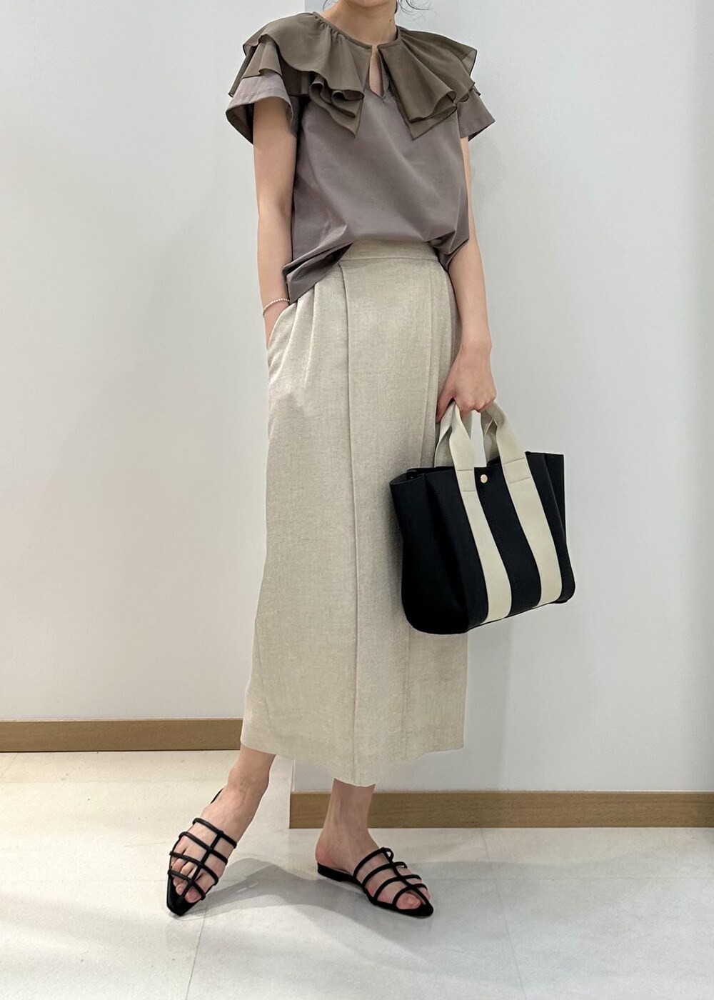 ブラック系のトートバッグ、ブラック系のサンダル、ベージュ系のTシャツ/カットソーを着用したレディースの夏コーディネートの4枚目の写真