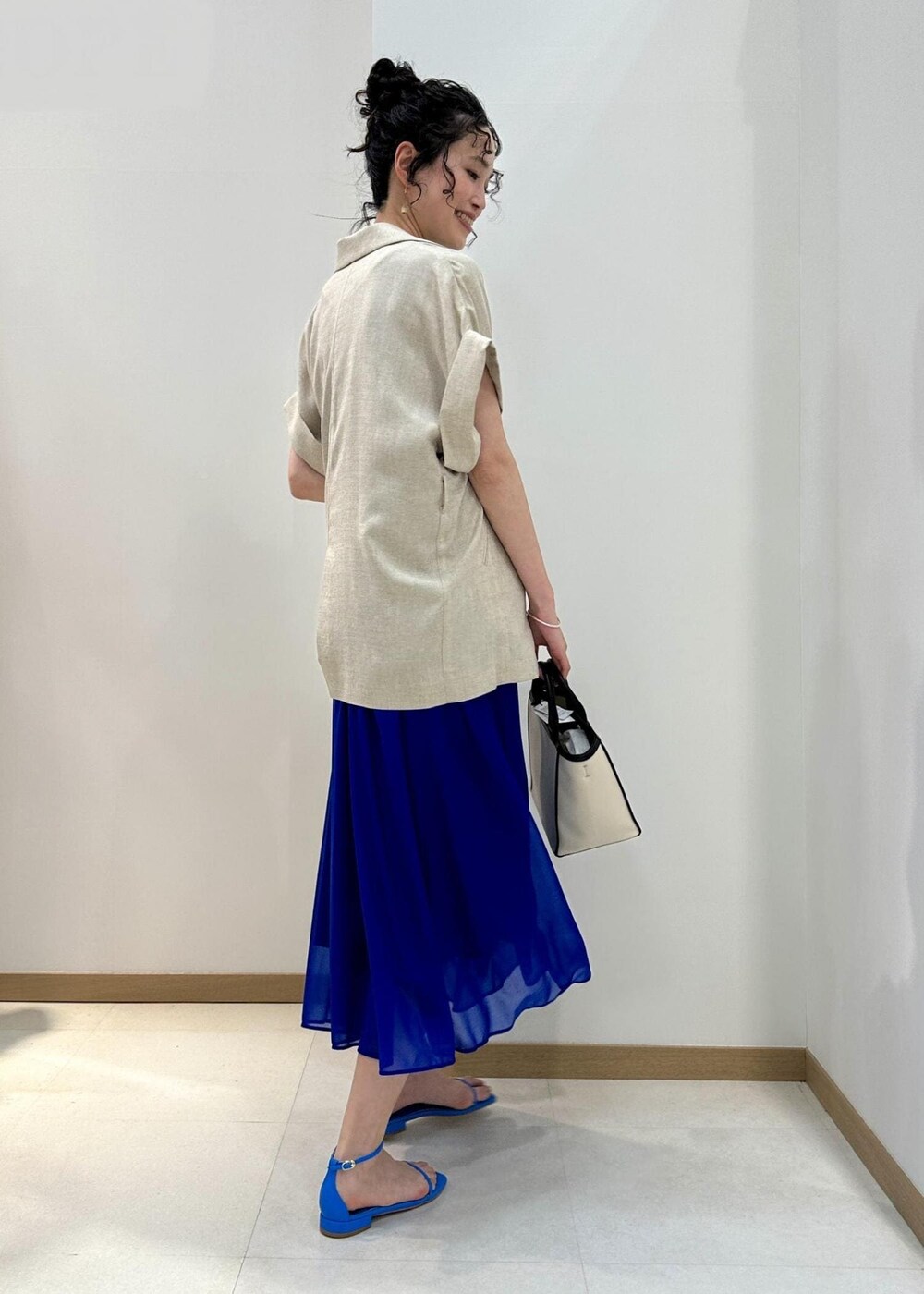 ブラック系のトートバッグ、ブルー系のサンダル、ブルー系のワンピースを着用したレディースの春コーディネートの3枚目の写真