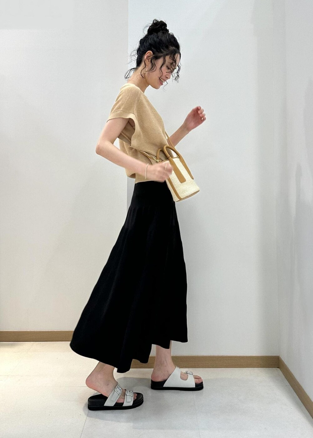 ベージュ系のハンドバッグ、ホワイト系のサンダル、ブラック系のスカートを着用したレディースの夏コーディネートの2枚目の写真