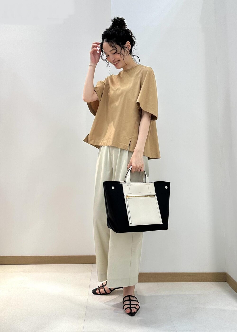 ブラック系のハンドバッグ、ブラック系のサンダル、ベージュ系のTシャツ/カットソーを着用したレディースの夏コーディネートの2枚目の写真