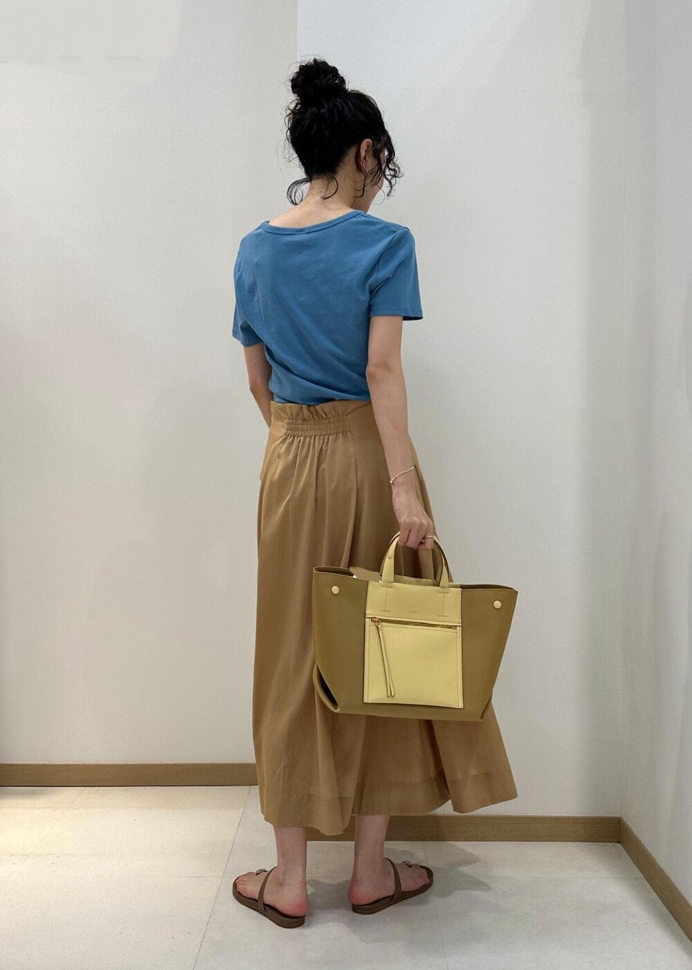 イエロー系のハンドバッグ、ベージュ系のサンダル、ベージュ系のスカートを着用したレディースの夏コーディネートの3枚目の写真
