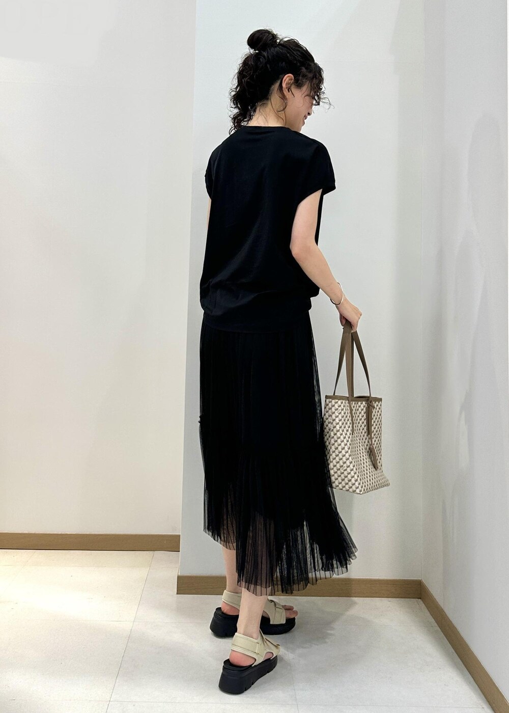 ベージュ系のトートバッグ、ホワイト系のサンダル、ブラック系のTシャツ/カットソーを着用したレディースの夏コーディネートの3枚目の写真