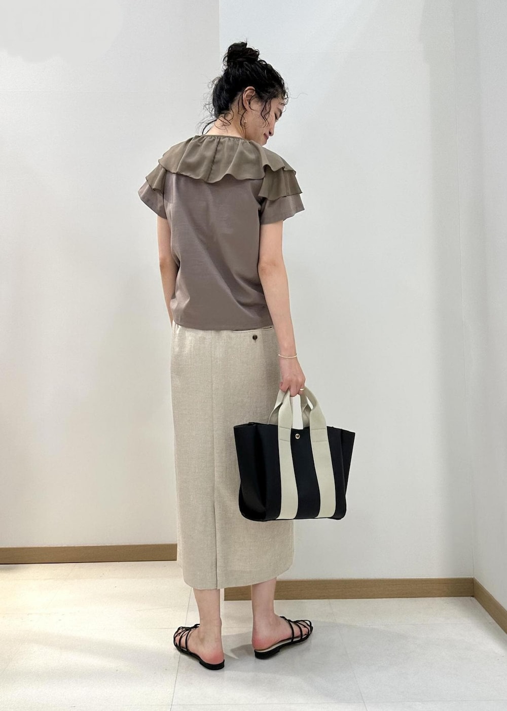 ブラック系のトートバッグ、ブラック系のサンダル、ベージュ系のTシャツ/カットソーを着用したレディースの夏コーディネートの3枚目の写真