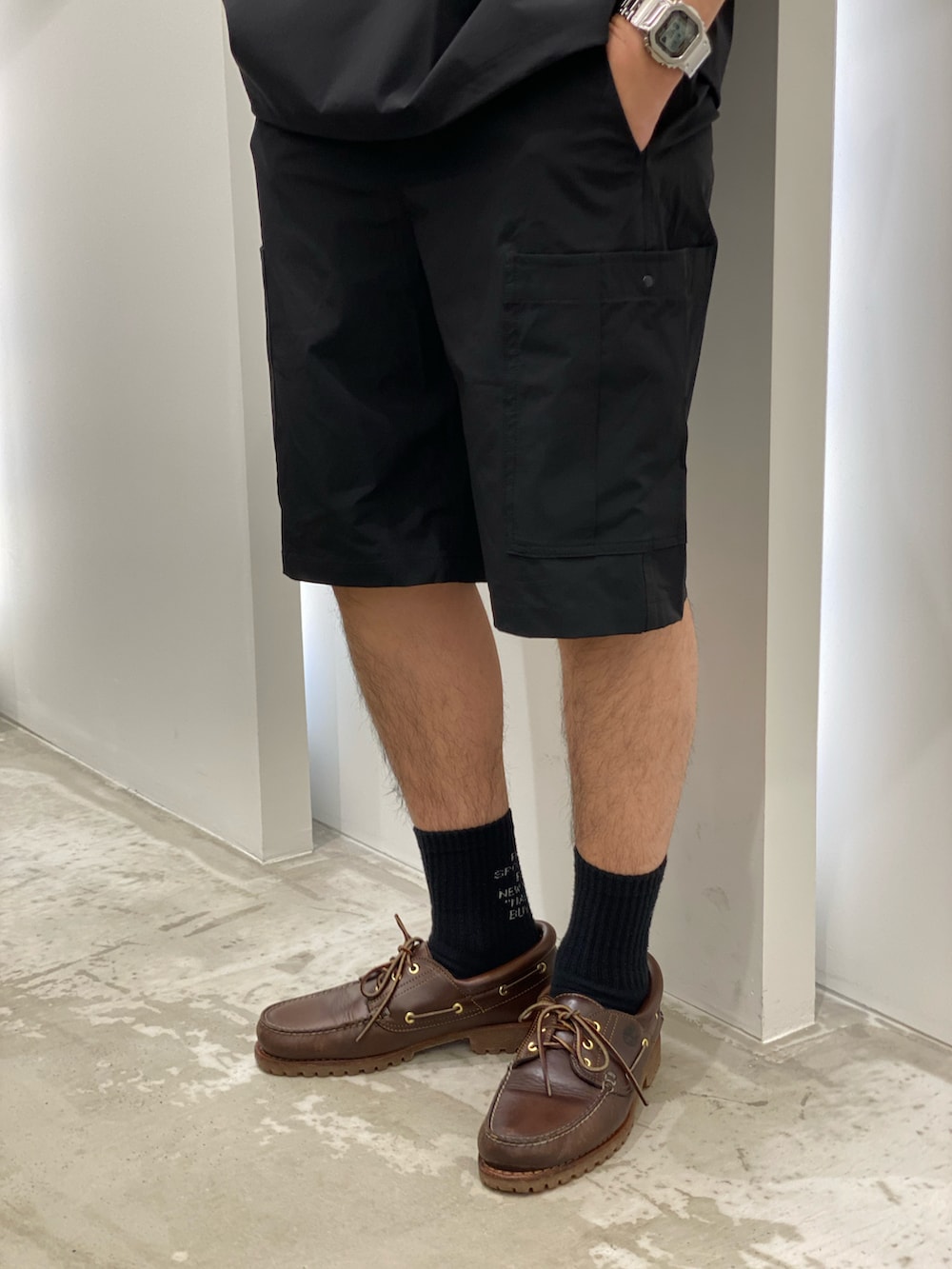 ブラック系のポロシャツ、ブラック系のパンツ、ブラウン系のモカシン/デッキシューズを着用したメンズの春コーディネートの3枚目の写真
