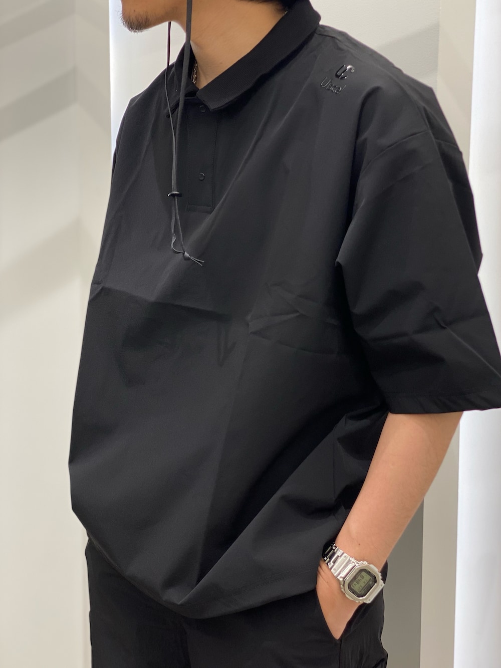 ブラック系のポロシャツ、ブラック系のパンツ、ブラウン系のモカシン/デッキシューズを着用したメンズの春コーディネートの2枚目の写真
